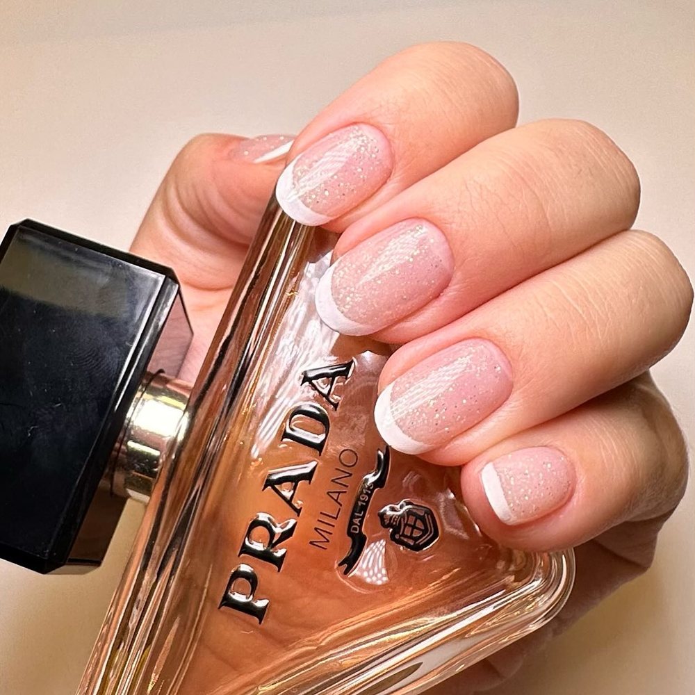 Unhas naturais com francesa e manicure russa, ao lado de um perfume