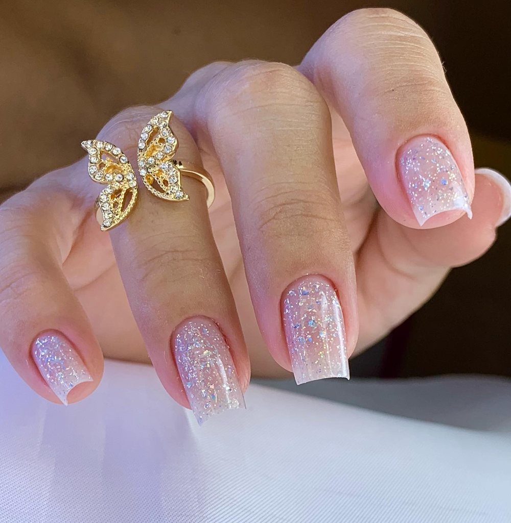 Alongamento em gel com glitter e ponta francesa, mão com anel de borboleta